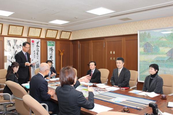 市長室で男性が立って資料を読んでいて、市長の右横の女性が手話で前に座っている3人に話をしている写真