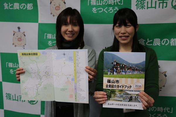 左側の女性はガイドブックの掲載騎乗位置図のページを広げて両手に持ち、右側の女性はガイドブックの冊子の表紙を見せて両手に持っている写真