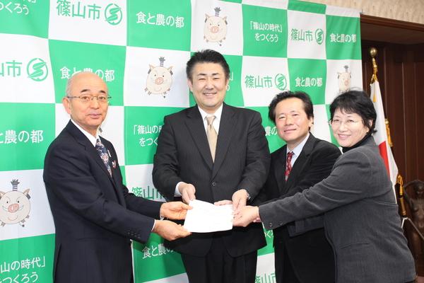 市長と男性2人と女性で、みんなで1枚の書類を持って記念写真