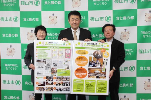 女性、男性2人がポスターの表紙を見せてる写真