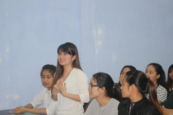 女子学生が7名ほど座っていて、一番前にいる髪の長い女性が立って話をしている写真