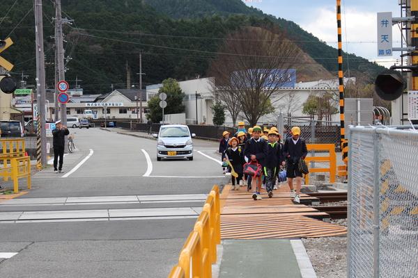 制服を着た小学生らが弁天踏切の歩道を歩いている横で車が走っている写真