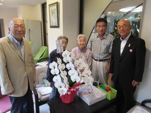長寿祝福者 松本マツヱさん(103歳)が市長年配の男性2名女性1名らとお祝いの胡蝶蘭と記念品を前に記念撮影している写真