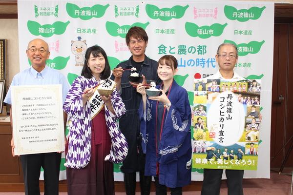 「丹波篠山コシヒカリ宣言」のパネルを持った市長と「丹波篠山コシヒカリ宣言」のポスターを持った男性と丹波篠山観光大使ら3名が箸でご飯をつまみあげてアピールしている写真