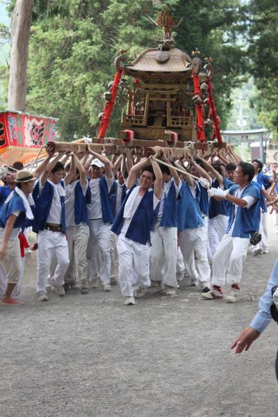神社の境内で大勢の男性陣がお神輿を担いでいる写真