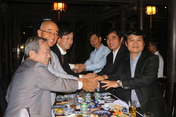 6名の男性達が、テーブルをはさんで3人ずつ縦に並んでいて、握手をしている写真