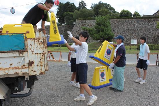 サインキューブ 「駐車禁止」をトラックに運んでいる体操服姿の生徒を受け取る男性で片付けている写真