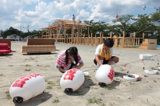 お祭りの舞台が解体され、飾られた提灯を外している男女の子供の写真