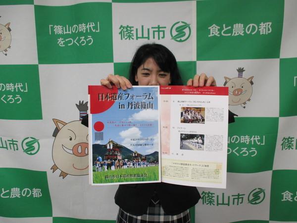 篠山市と書かれた幕の前で、女性が「日本遺産フォーラムin丹波篠山」と書かれたパンフレットを広げている写真
