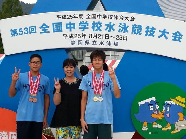 競技大会の案内板の前で選手2人と親が一緒にピースサインをして記念撮影