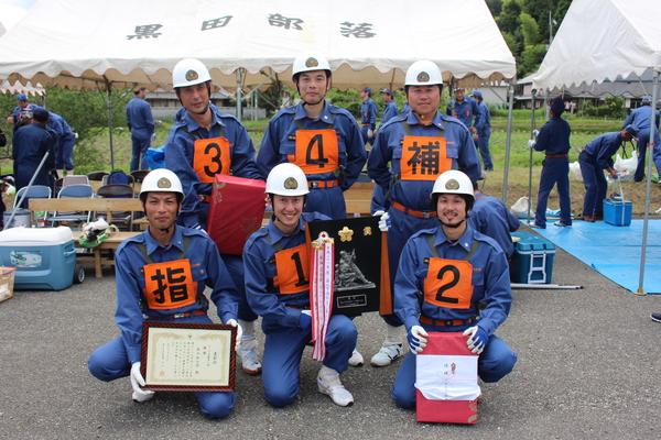 6名の団員が前列と後列で、景品と賞状と表彰盾を持っている写真