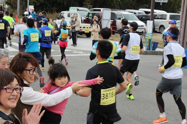選手たちが走っている中、沿道でお母さんに抱っこされている女の子がタッチしようとしている写真
