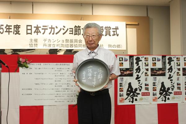 酒井 修さんが、印字されたプレートを持ち立っている写真