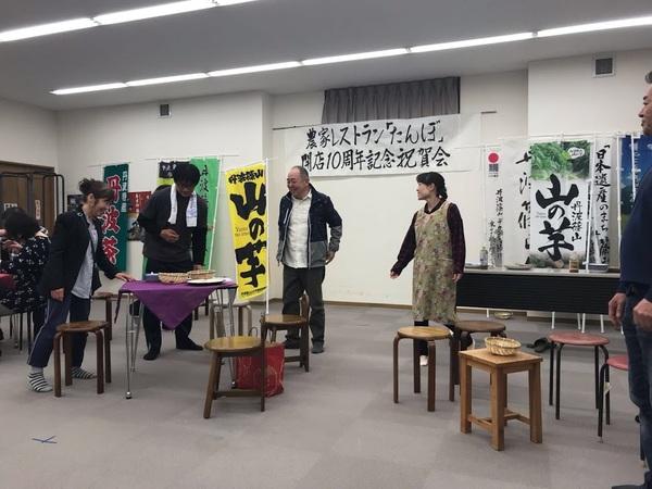 農家レストランたんぼ開店10周年記念祝賀会と書かれた紙が壁に貼ってあり、山の芋と書かれたのぼり旗が飾ってある部屋に6名ほどの人達が立っている写真