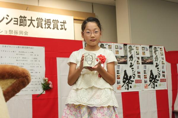 胸章リボンをつけた岸田 奈侑さんが、豚の絵が描かれた白いマグカップを持っている写真
