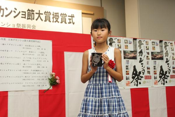 胸章リボンをつけたワンピースを着た内藤 心深さんが黒いマグカップを持っている写真