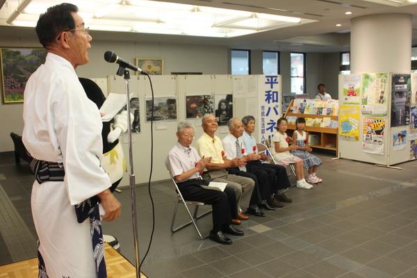 浴衣を着た男性が、紙を片手に歌っている姿を椅子に座りながら鑑賞している受賞者の写真