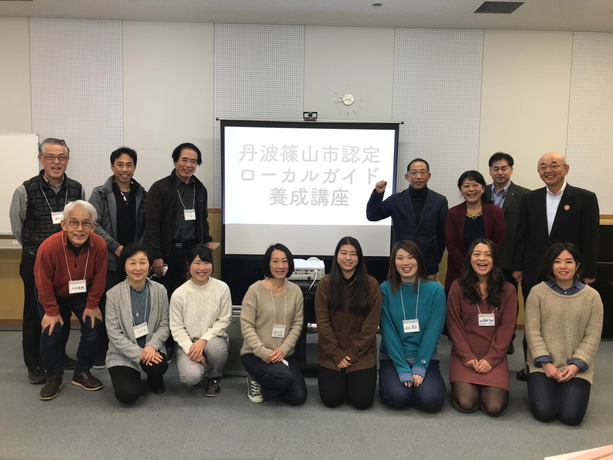「丹波篠山市認定ローカルガイド養成講座」と表示されたスクリーンを囲って1列目が中腰で、2列目の方は立って記念撮影