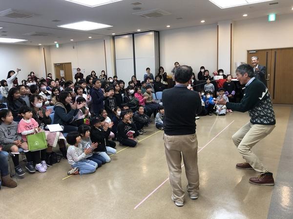 沢山の子供たちの前で、男性二人が何かを披露している写真