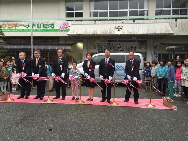 赤いカーペットの上で代表の男の子と大人たちがテープカットをする写真