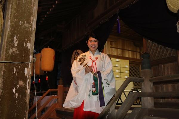 神社で巫女が神楽鈴を持って笑顔で写っている写真