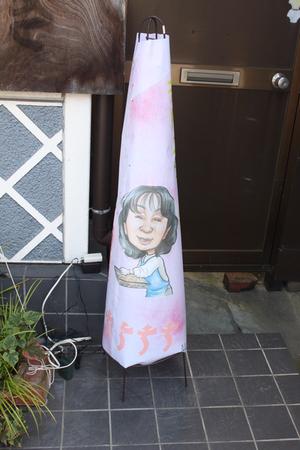 ドアの前にエプロンを着た女性が描かれたあんどんが置いてある写真