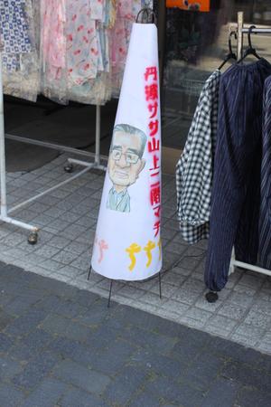 洋服屋の店の前にメガネをかけた年配の男性が描かれたあんどんが置いてある写真