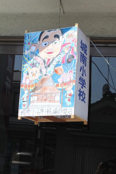 小学6年生の磯貝くん作の市長と市のキャラクターの描かれた灯篭がドアの前にかけられている写真