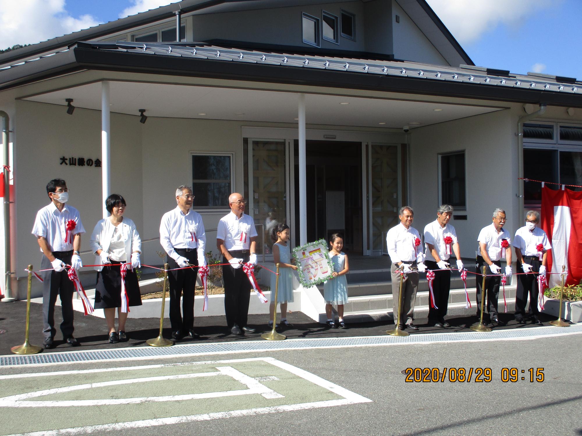 施設までテープカットを行う出席者、中央には「祝」というプレートを持ったこども2人