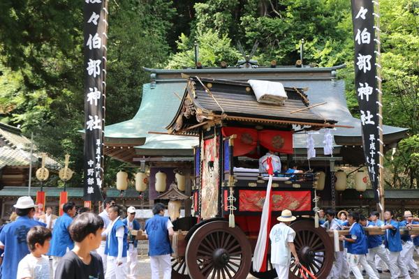 神社にて子供らが乗った山車を法被姿の男性らが押している写真