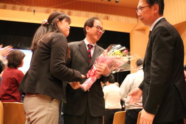 現職員さんの間を、花束を持った退職者が通っていく写真