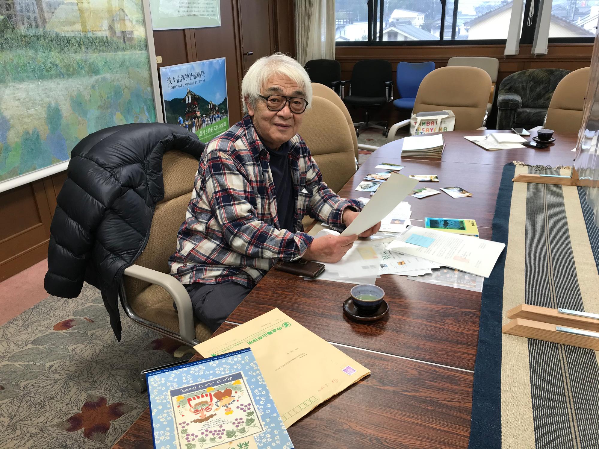 机に森の学校にかかわる秘蔵資料を並べて、西垣監督が椅子に座られている。