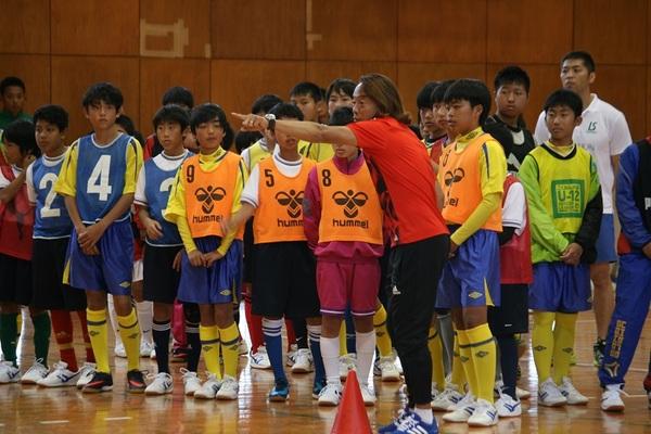体育館で北澤選手が指をさして説明しているのを見ている子供たちの写真
