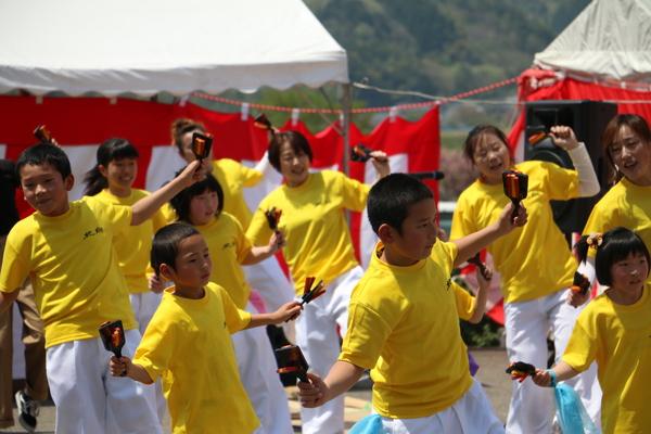 黄色いティシャッに白いズボンをはいた子供達が鳴子を手に持ち踊っている写真