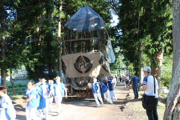 神社の境内で法被姿の男性らがキュウリ山を押している様子を見ている人々の写真