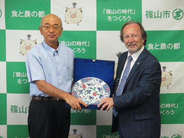 市長と陶芸家の男性が丸い陶芸のお皿を二人で持って並んでいる写真