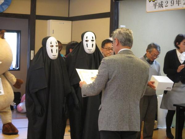 かおなし」の仮装をしている2人が、グレーの背広を着た男性に、賞状を読んでもらい表彰を受けている様子の写真
