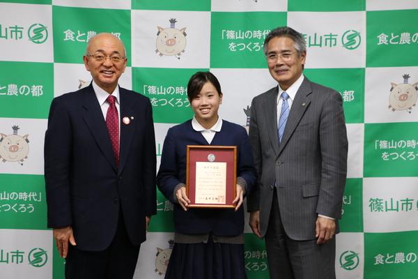 賞状をもった井上真帆さんがをはさみ市長、先生と三人で記念写真