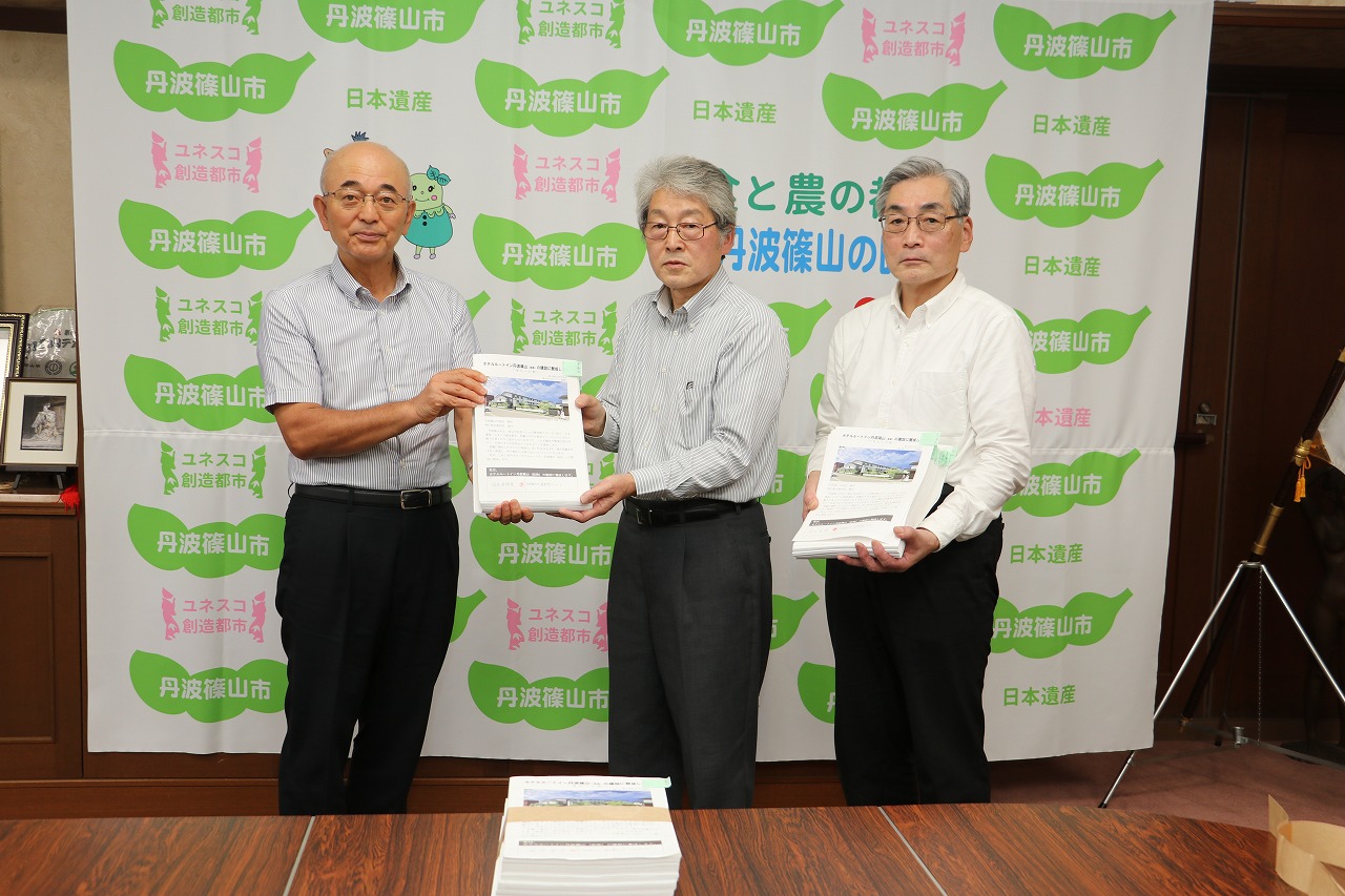 小山会長から、酒井市長へ署名の一部を手渡している。小山会長の横で藤本会長が署名の一部を持っておられる。手前の机に、残りの署名の束が置いてある。