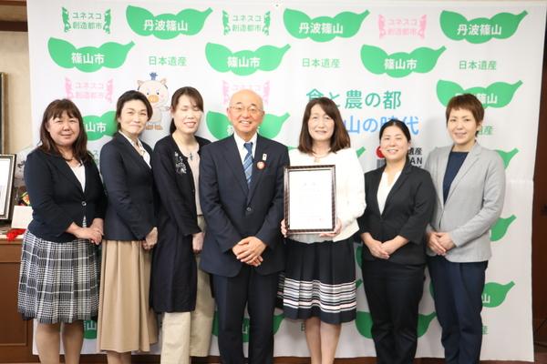 市長を真ん中に賞状を持った女性1名と他5名の女性が微笑みながら立っている写真