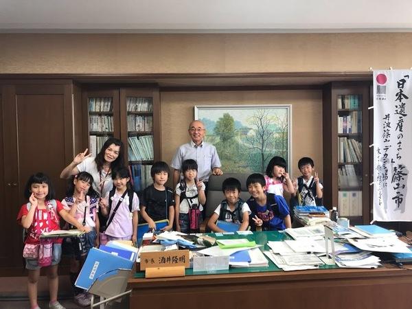市役所庁舎の見学に訪れ市長室で西紀地区の小学3年生9名と先生と市長が笑顔でピースサインをしている写真