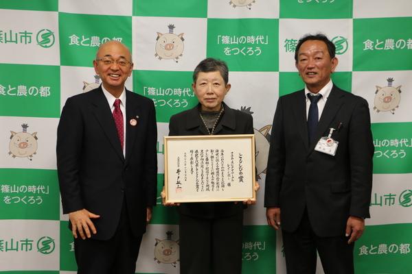 ともしびの賞の賞状を持って、阪下千代美さんと市長と関係者で記念写真