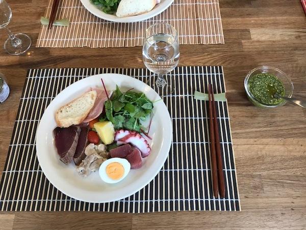 肉・魚・野菜・卵・パンなどが一つの皿に盛り付けられている横にジェノベーゼソースが置いてある写真