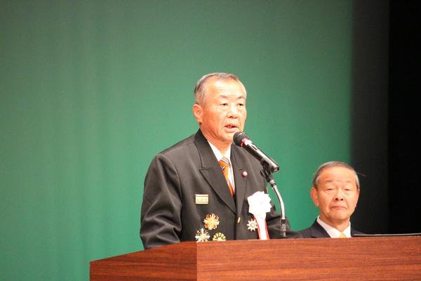 勲章がついている制服姿の北山団長が壇上で挨拶をしている写真
