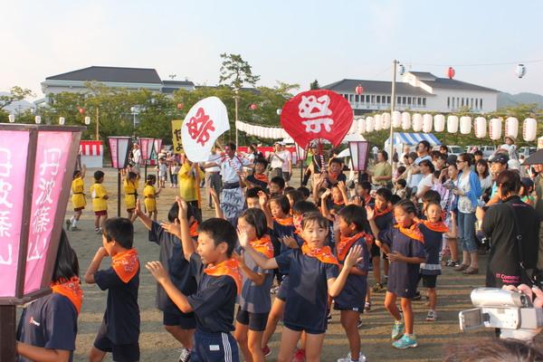首にオレンジ色のバンダナを巻き、元気よく踊る子供たちの写真