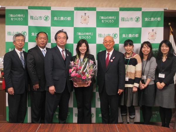 谷掛さんが花を持って、市長、職員で記念写真