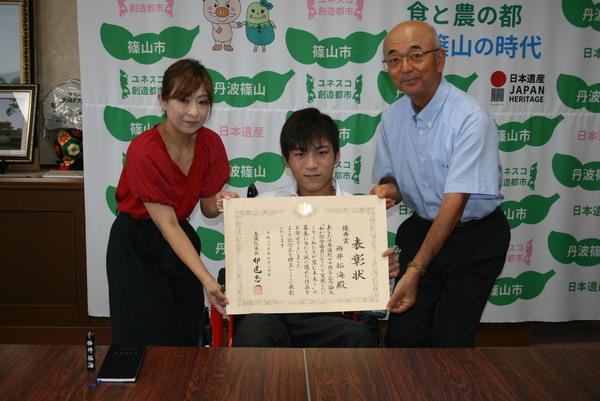 西井 拓海さんが持っている賞状をその両端で女性と市長が一緒に支えている写真