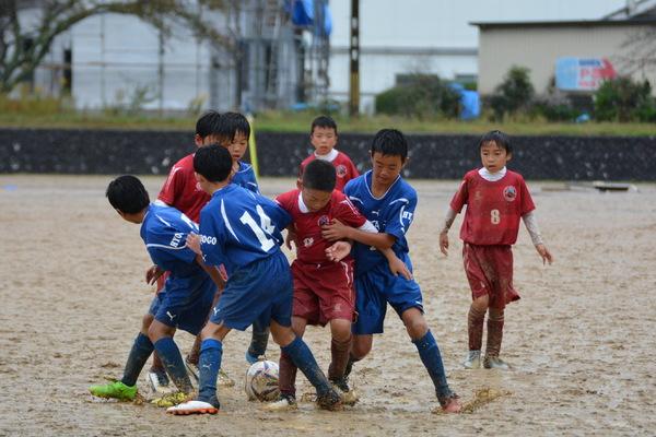 雨の中、7人の少年たちがサッカーをしていてボールを足で取り合っている写真