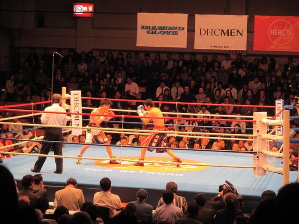 角谷 淳志選手とチャンピオン拳四朗（けんしろう）選手の試合の様子を観客席から見ている写真
