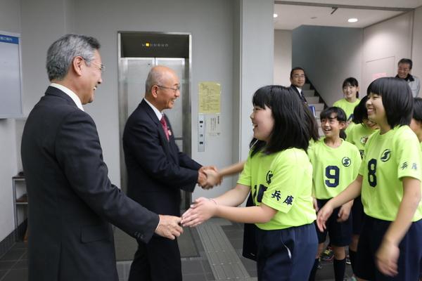 「第1回全日本女子総合選手権兵庫県大会」で見事優勝し全国大会への出場権を獲得した小学生女子のドッチボールチーム「Colorsささやま」のメンバーがユニホーム姿で市役所を訪問し笑顔で市長と握手を交わしている写真